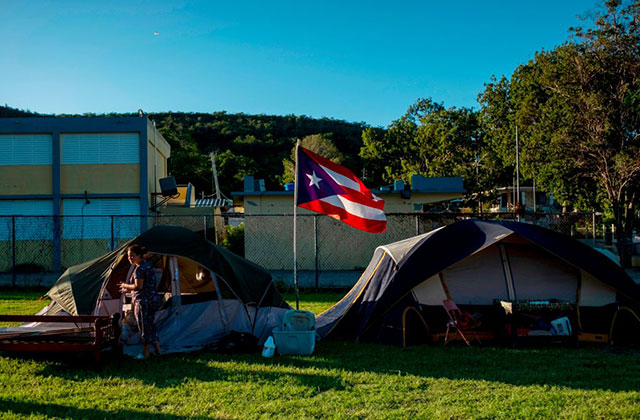 Person stands in front of two tents on a field with the Puerto Rican flag flying in between.