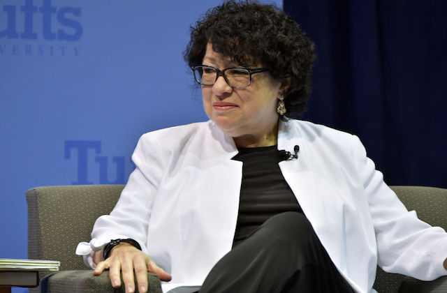 Justice Sonia Sotomayor. A Latinx woman wears a black shirt, black pants and a white blazer as she sits in a gray chair.