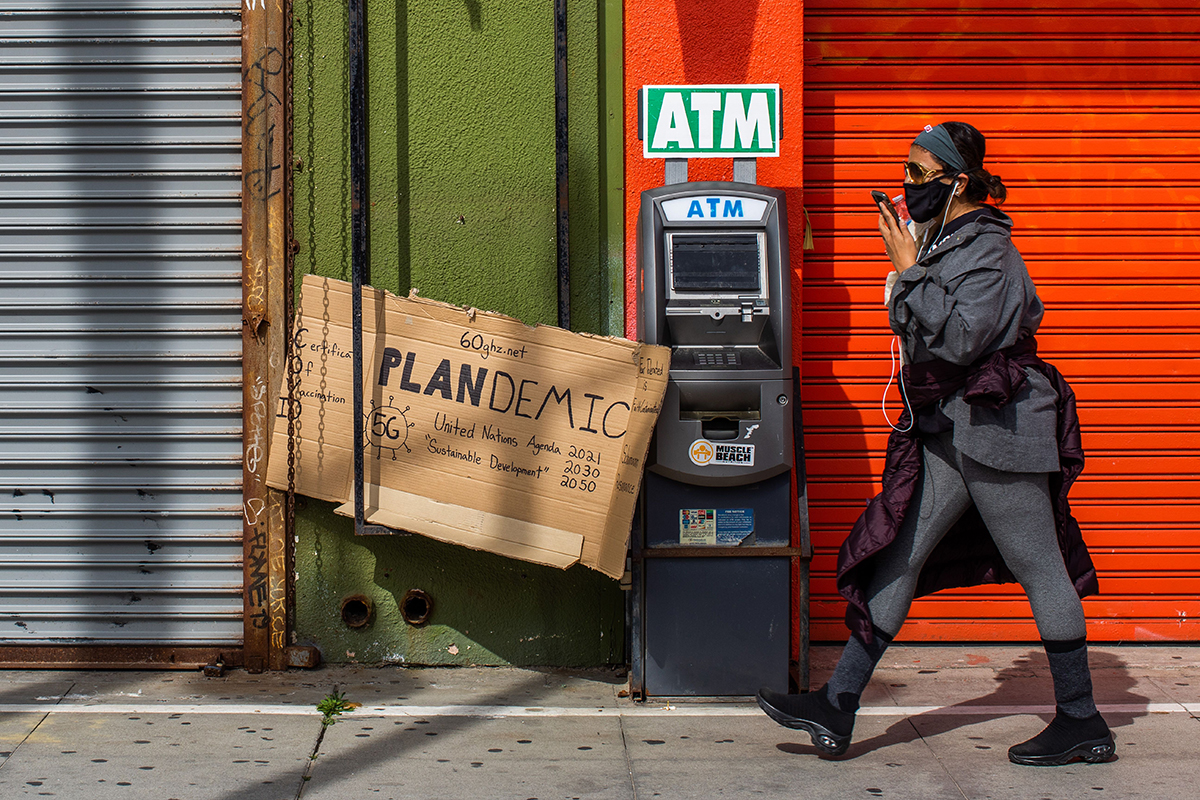 A young black woman dressed in gray and wearing a black mask, walks by the closed stores of the Boardwalk in Venice, California .