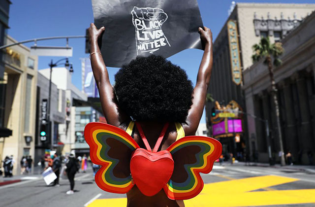 Strike for Black Lives. Black woman with big dark Afro holding a 'Black Lives Matter' sign and waring a heart shaped, butterfly shaped backpack.