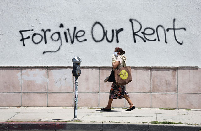 Unaffordable-Rent. Woman wearing mask walks passed spray painted message reading Forgive Our Rent.