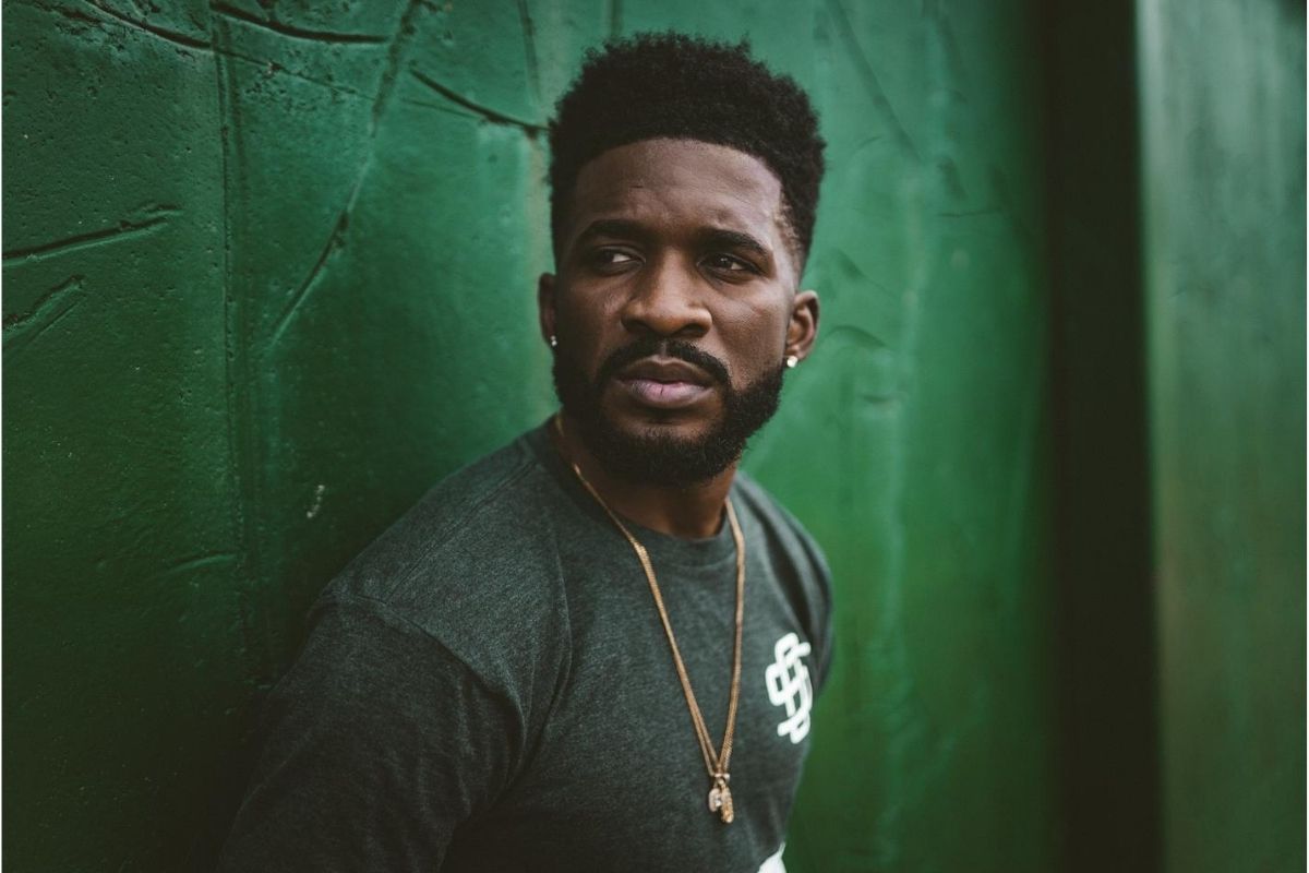 Black man, in his 30s, looking to the side behind a jade green wall.