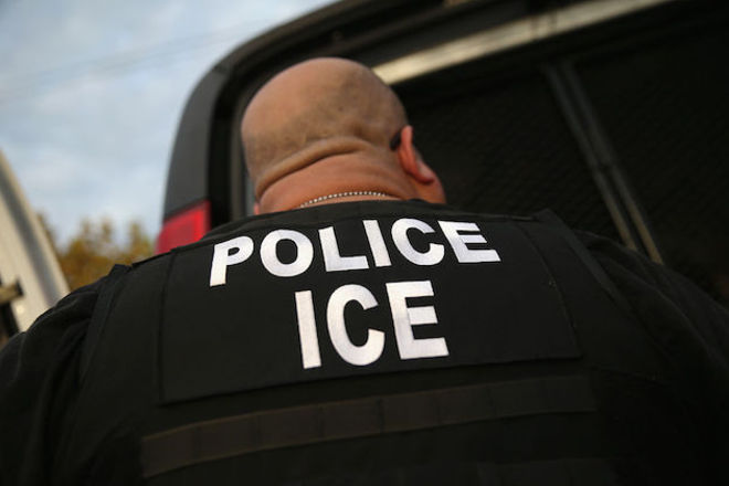 Close-up of the back of an agent wearing a black jacket with the words police ICE written in large, white letters. 