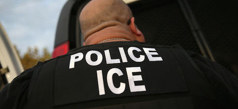 Close-up of the back of an agent wearing a black jacket with the words police ICE written in large, white letters. 