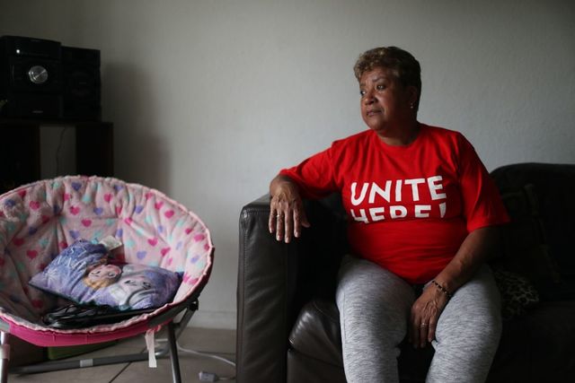 Brown-skinned Latinx woman sitting on a couch, with short salt and pepper hair, looking off into the distance