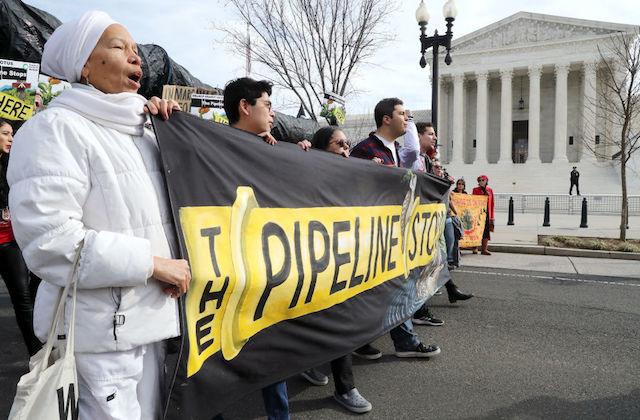 A line of activists stand in front of Supreme Court holding a banner that reads "The Pipeline Stops"