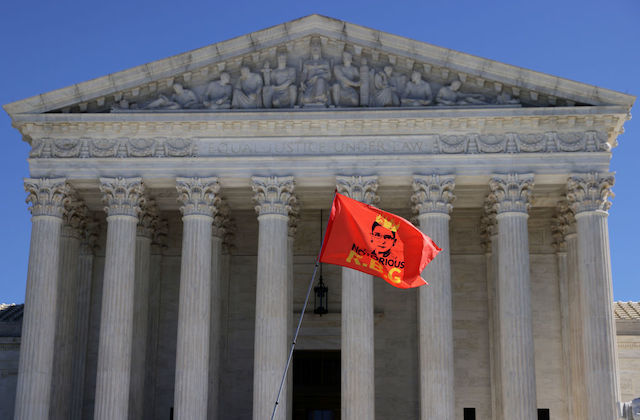 The Supreme Court stands in the background as a red flag with a drawing of Justice Ruth Bader Ginsberg and the words Notorious RBG flies in the foreground.