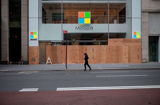 Microsoft. Boarded up storefront with windows logo  and person wearing all black running by.