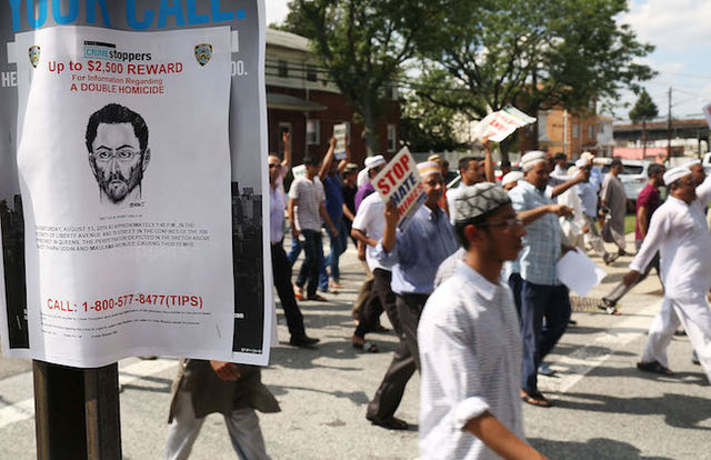 White poster with black lettering and image on a brown post, men in multi-colored outfits in background