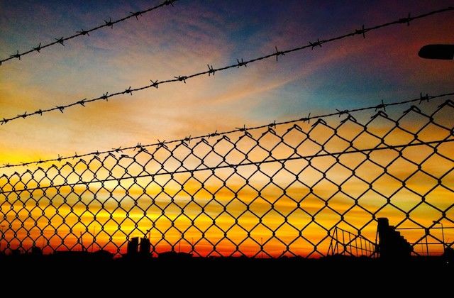 Barbed wire surrounding a prison during sunset.