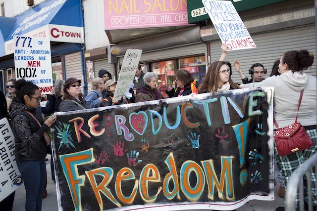 A multiracial group of women hold up a colorful sign that says, “Reproductive Freedom!”