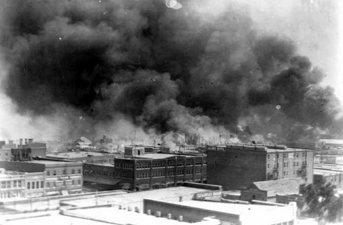 Black-and-white photo of black and brown buildings against grey sky with black smoke