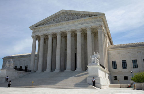 Supreme Court. White building with multiple white pillars and multiple steps. Guards stand on stairs.