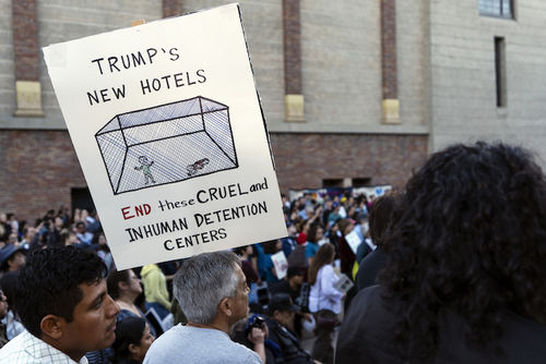 A demonstrator holds up a hand drawn sign of an immigration cage with the caption "Trump's new hotels."
