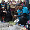 A Native man wearing a turquoise t-shirt prays while a group watches
