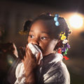 A little Black girl wearing colorful barrettes holds a rag in front of her mouth to block police tear gas during a protest against the killing of Michael Brown