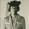 Sepia image of Black woman in black-and-white patterned dress and hat in front of brown background