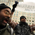 A black man wearing a black vest holds up a sign that says "Net neutrality affects us all."