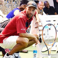 James Blake. Black man in red polo shirt, white shorts, black hat