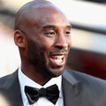 Kobe Bryant. Black man in black and white tuxedo in front of red and white background.