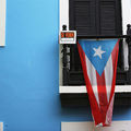 A Puerto Rican flag hangs from a black-shuttered window set in a bright blue exterior wall