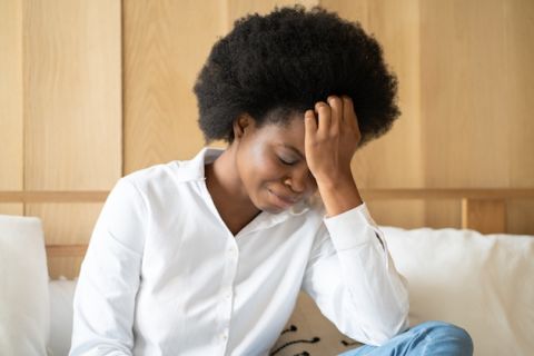 Black woman with an afro faces down with hand on forehead, looking depressed.