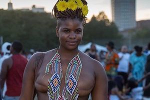 Black woman with yellow flowers in her hair, a beaded necklace and two mastectomy scars