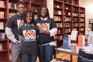 A Black man and a Black woman pose with a pre-teen Black child in a bookstore