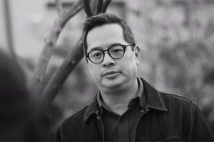 We Gon' Be Alright. Asian man with short dark hair, round black framed glasses, dark button shirt and dark jacket.